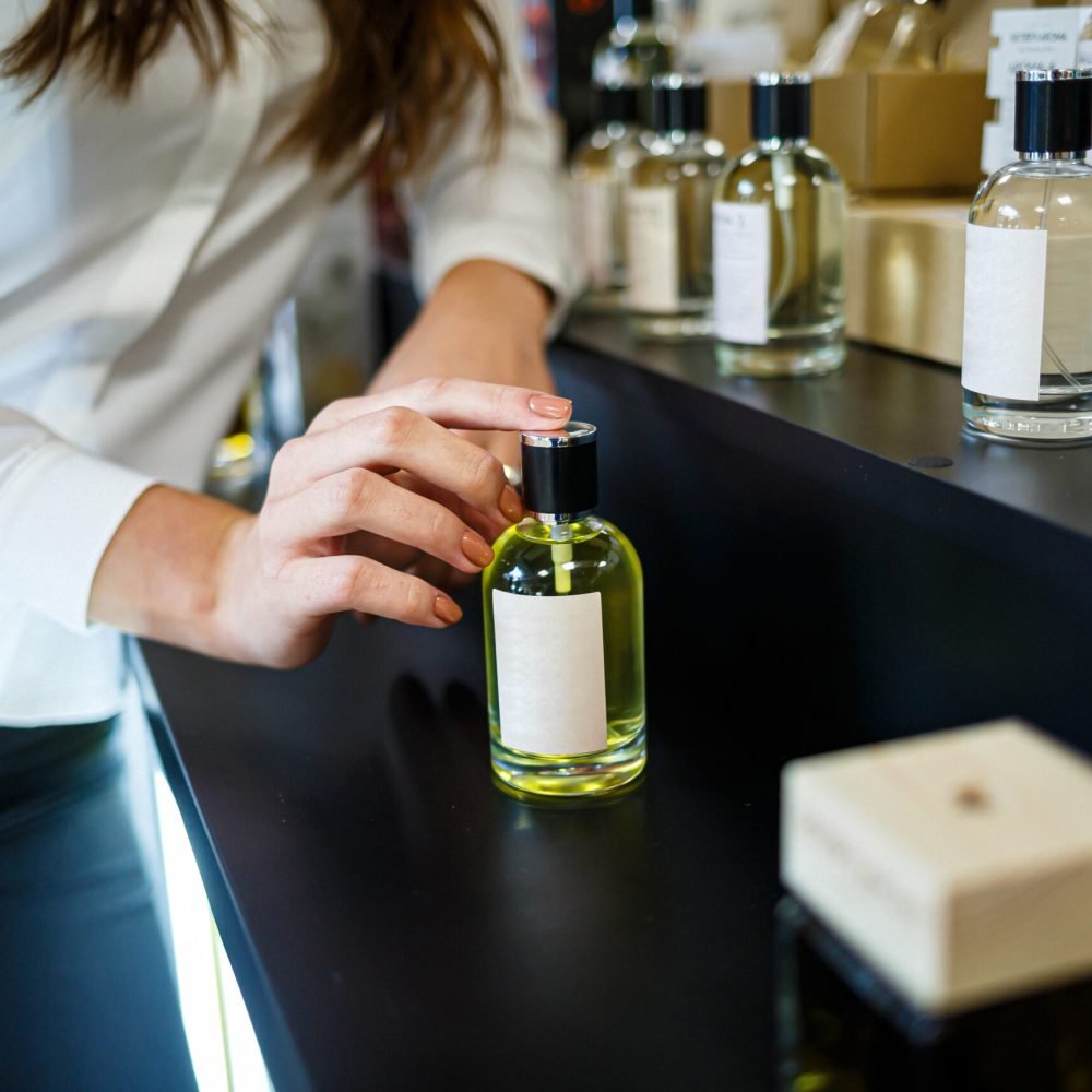 Bottle perfume female hand. Young woman holding bottle of perfume. Fashionable perfumes in hands of women. Girl sprays perfume. Beautiful women's hands.